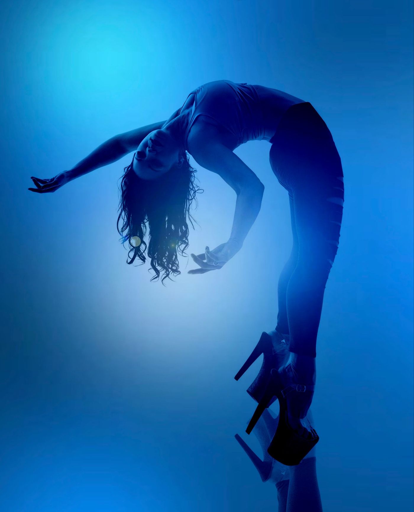Dancer in a deep backbend under blue studio light