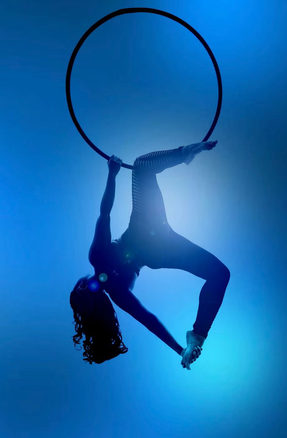 Aerialist silhouetted inside a Lyra hoop under blue light