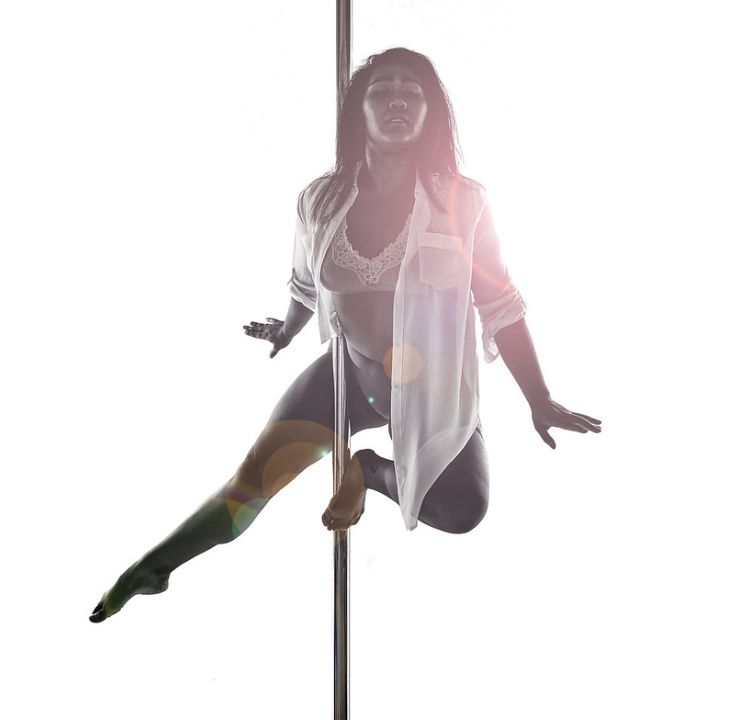 Dancer seated on a pole in bright studio light